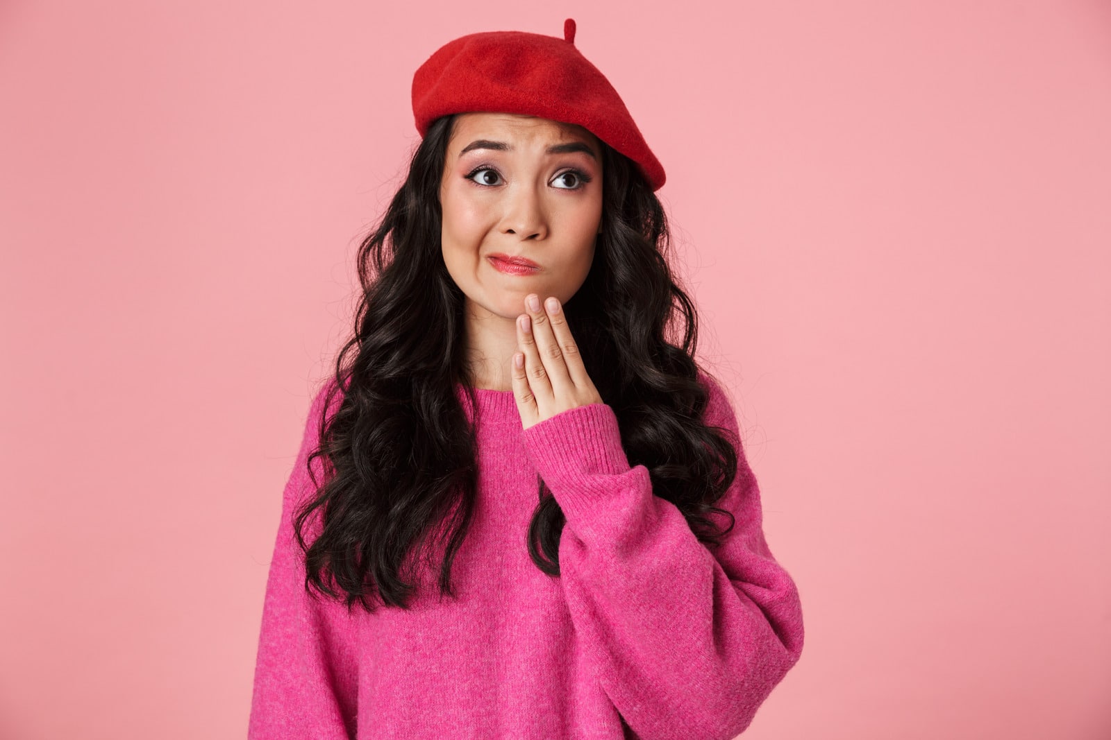 Image of thoughtful asian woman with long dark hair wearing beret thinking or hesitating isolated over pink background